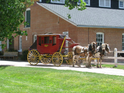 A red horse-drawn carriage parked in front of a brick building, with two horses harnessed to it on a grassy area.