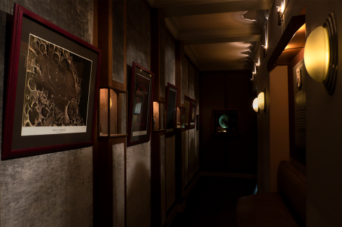 A dimly lit hallway featuring framed artwork on the walls and soft wall sconces illuminating the space.