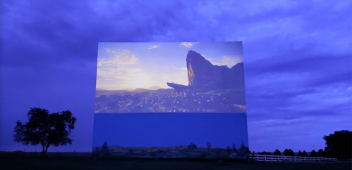 A large outdoor screen displays a scenic landscape at dusk, with a rocky formation and a colorful sky.