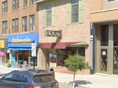 A brick building with a sign for "Off The Vine" and a colorful storefront for "artmain" nearby.