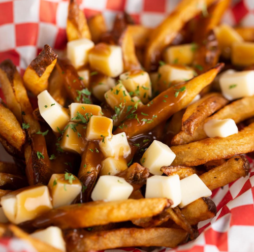 A close-up of golden fries topped with cheese curds and gravy, served in a red and white checkered basket.