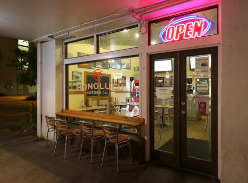 A brightly lit burger restaurant with an "OPEN" sign, featuring outdoor seating and a welcoming atmosphere.