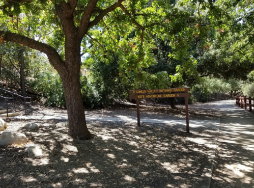 Sign for Conejo Valley Botanic Garden, surrounded by trees and a pathway leading to the Kids' Adventure Garden.
