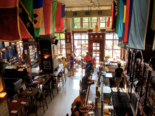 A lively pub interior with colorful flags, patrons at the bar, and tables filled with people enjoying their meals.