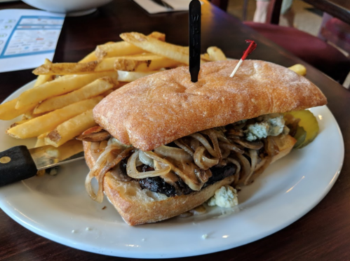 A sandwich with grilled onions and blue cheese, served with a side of golden fries on a white plate.