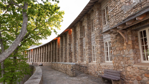 A curved stone building with large windows, surrounded by greenery and a stone pathway.