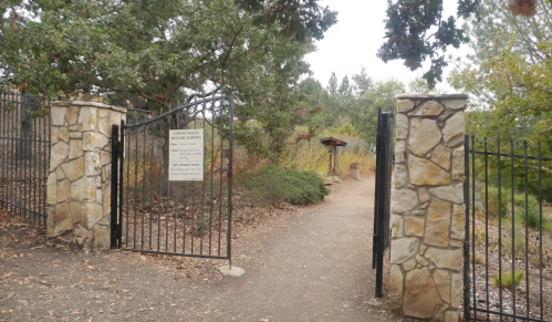 A stone gate opens to a dirt path leading into a garden, surrounded by trees and greenery.