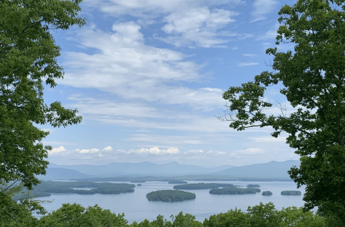 A scenic view of a lake surrounded by islands, with mountains in the background and a partly cloudy sky.