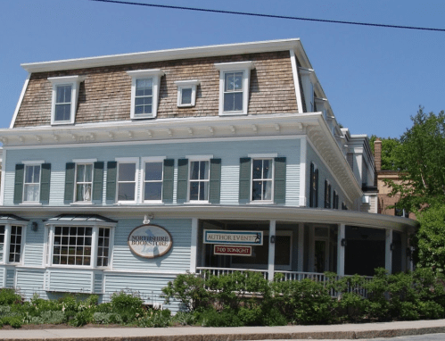 A charming blue building with white trim and green shutters, featuring a sign for an author event.