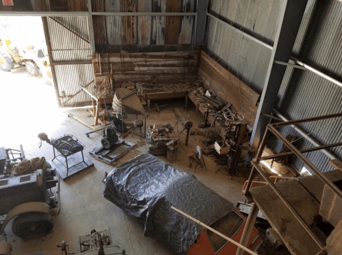 A cluttered workshop with various tools and machinery scattered around, viewed from an upper level.