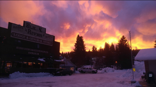 A vibrant sunset with orange and purple clouds over a snowy landscape, featuring a lodge and general store.