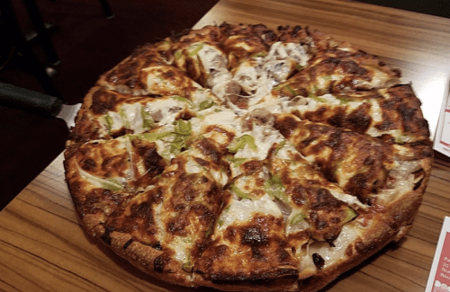 A freshly baked pizza with melted cheese, green peppers, and toppings, sliced into eight pieces on a wooden table.