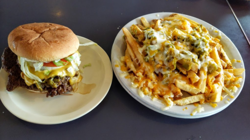 A cheeseburger with lettuce and tomato next to a plate of loaded cheese fries topped with jalapeños.