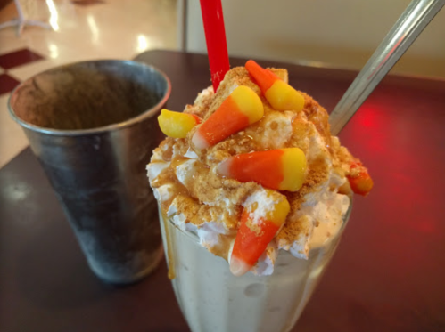 A creamy milkshake topped with whipped cream, crushed cookies, and candy corn, served with a red straw.