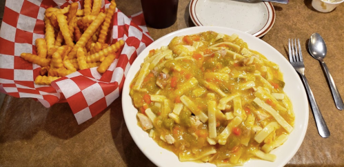 A plate of chicken and vegetable stew with noodles, alongside a basket of crinkle-cut fries and a drink.