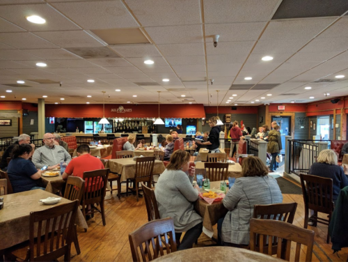 A busy restaurant interior with diners at tables, a bar area, and staff serving customers.