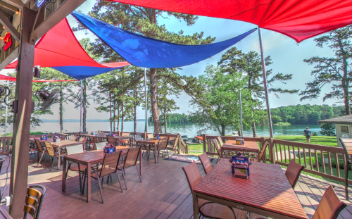 Outdoor dining area with colorful canopies overlooking a lake, surrounded by trees and a peaceful atmosphere.