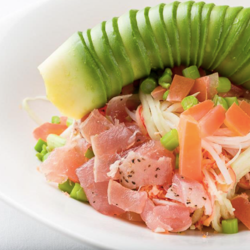 A colorful salad with shredded vegetables, diced ham, and a cucumber garnish on top.