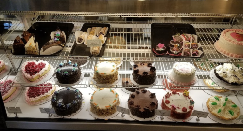 A display case filled with various cakes, including chocolate, fruit, and decorated options, all beautifully arranged.