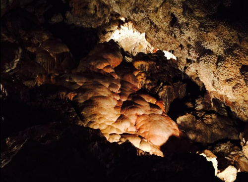 Stalactites and stalagmites illuminated in a dark cave, showcasing unique rock formations and textures.