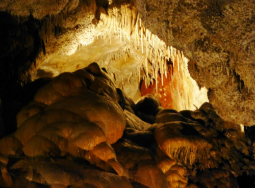 Stalactites and rock formations in a dimly lit cave, showcasing natural textures and colors.