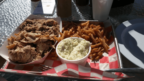 A tray with pulled pork, coleslaw, and crispy fries on a checkered paper.