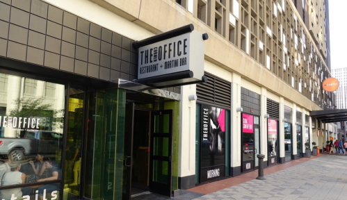 Exterior view of "The Office" restaurant and martini bar, featuring a modern entrance and nearby storefronts.