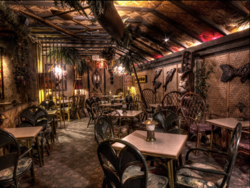 Cozy, dimly lit restaurant interior with tropical decor, bamboo furniture, and a warm ambiance.