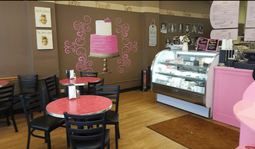 Cozy café interior with pink tables, a cake display, and a decorative cake mural on the wall.