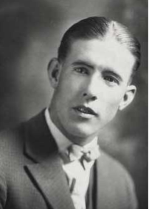 A black and white portrait of a young man in a suit, with slicked-back hair and a serious expression.
