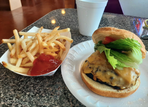 A cheeseburger with lettuce and tomato next to a serving of French fries and ketchup on a plate.