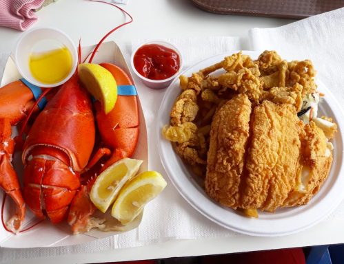 A plate featuring a lobster with lemon, and a fried chicken sandwich with fried seafood and ketchup on the side.