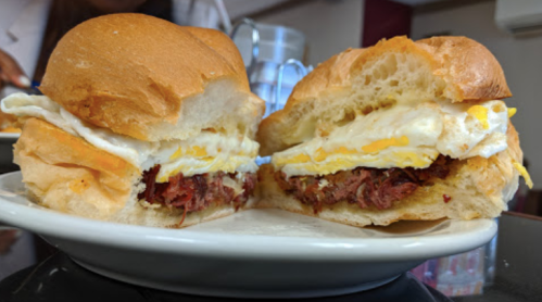 A close-up of a sandwich with layers of meat and a fried egg, served on a soft bun, on a white plate.