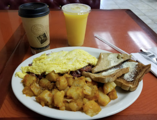 A plate of breakfast with scrambled eggs, potatoes, toast, a coffee cup, and a glass of orange juice on a table.