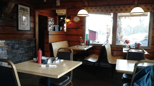 Cozy diner interior with wooden walls, tables, and chairs, featuring condiments and flowers on the tables.