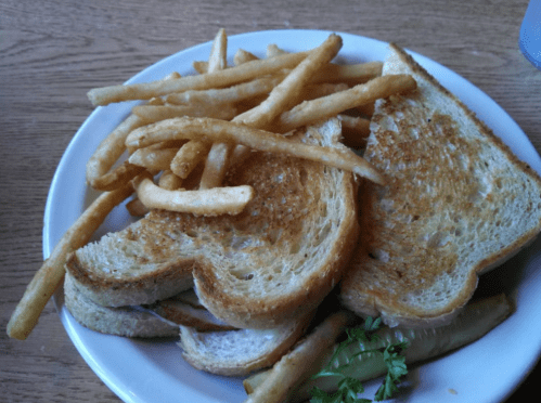 A plate with two grilled cheese sandwiches, a side of French fries, and a pickle slice garnished with parsley.