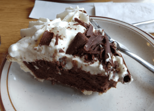 A slice of chocolate cream pie topped with whipped cream and chocolate shavings on a plate.