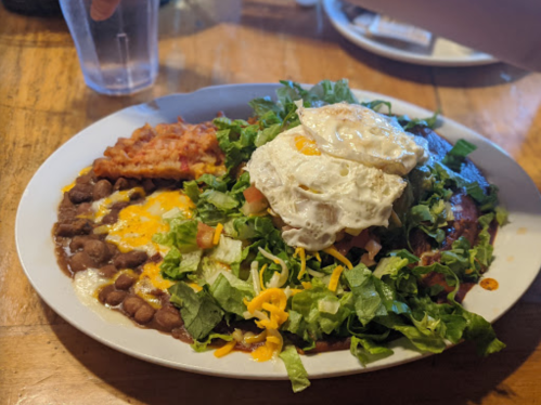 A plate of food featuring beans, cheese, lettuce, tomatoes, and two fried eggs on top, with a side of hash browns.