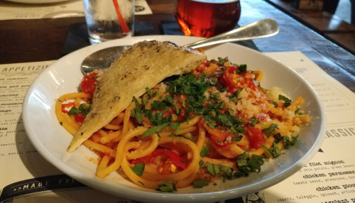 A bowl of spaghetti topped with tomato sauce, herbs, and a slice of bread, served on a wooden table.