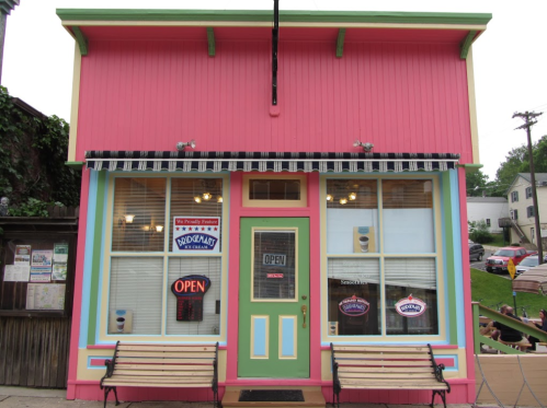 Colorful storefront with pink and green accents, large windows, and an "OPEN" sign. Benches are placed outside.