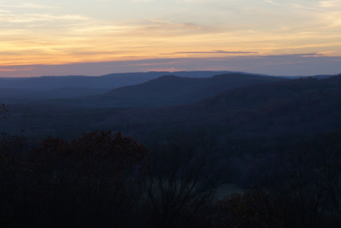 A serene landscape at sunset, featuring rolling hills and a colorful sky with soft clouds.