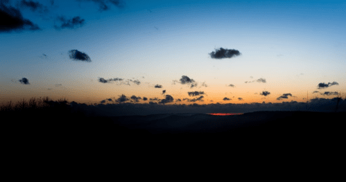 A serene sunset over rolling hills, with a gradient sky transitioning from blue to orange, dotted with clouds.