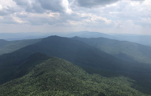A panoramic view of lush green mountains under a cloudy sky, with layers of hills fading into the distance.
