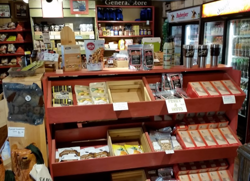 A rustic general store display with shelves of snacks, drinks, and various packaged goods.