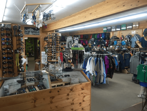 Interior of a retail store displaying outdoor gear, clothing, and accessories, with wooden accents and organized shelves.