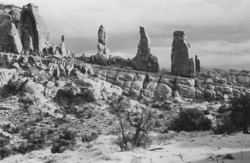 Black and white landscape featuring towering rock formations and rugged terrain under a cloudy sky.
