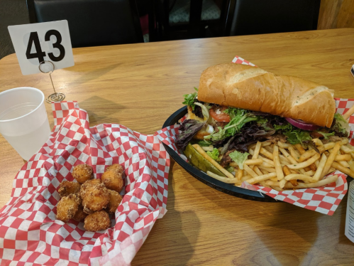 A large sandwich with lettuce and tomatoes, a side of fries, and a basket of fried snacks on a wooden table.
