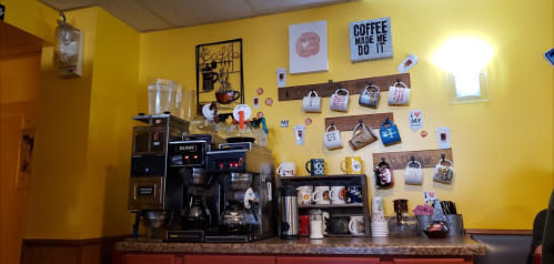 A cozy coffee station with a coffee maker, mugs hanging on the wall, and cheerful decor in a bright yellow setting.