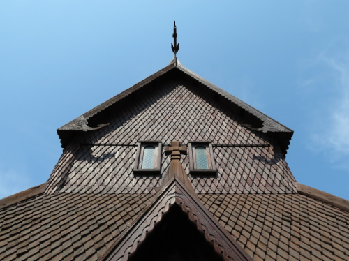 A close-up view of a wooden roof with intricate shingles and two small windows against a clear blue sky.
