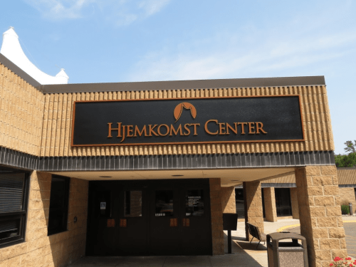 Sign for Hjemkomst Center on a building with a clear blue sky in the background.
